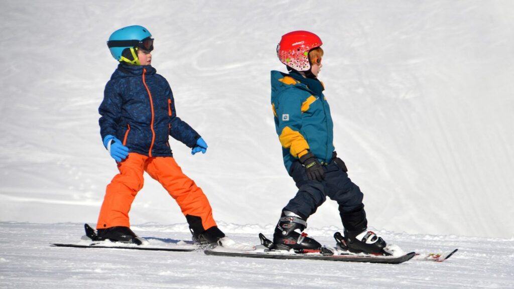 Two beginner skiers going down a groomed run together.