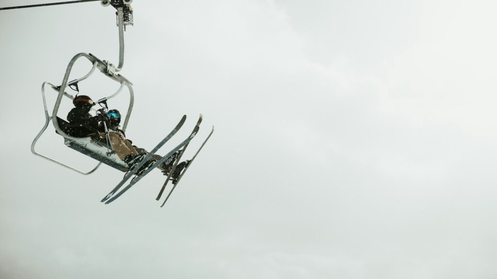 Two skiers riding on a chair lift on a cloudy day.