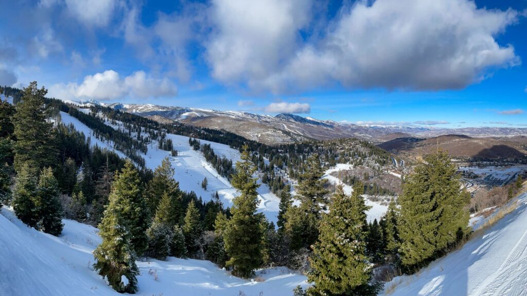 Deer Valley ski slopes surrounded by tall green trees and partially cloudy skies above.