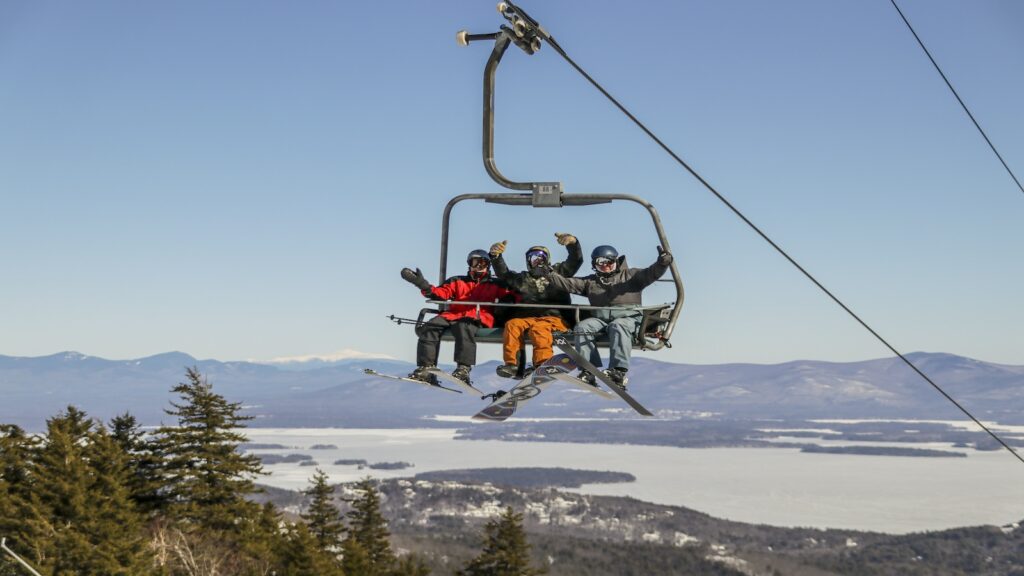 Skiers and a snowboarder on a chair lift at Gunstock Mountain.