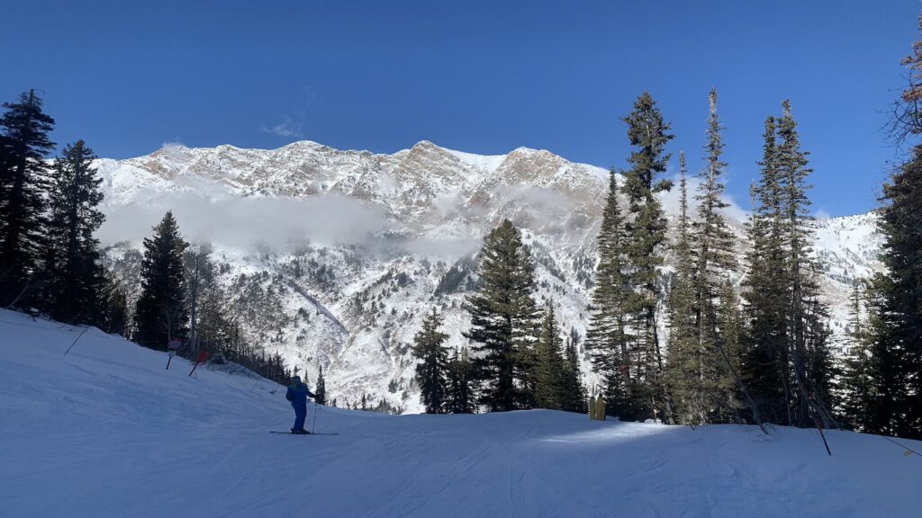 A skier at Snowbird with mountains and blue skies in the distance.