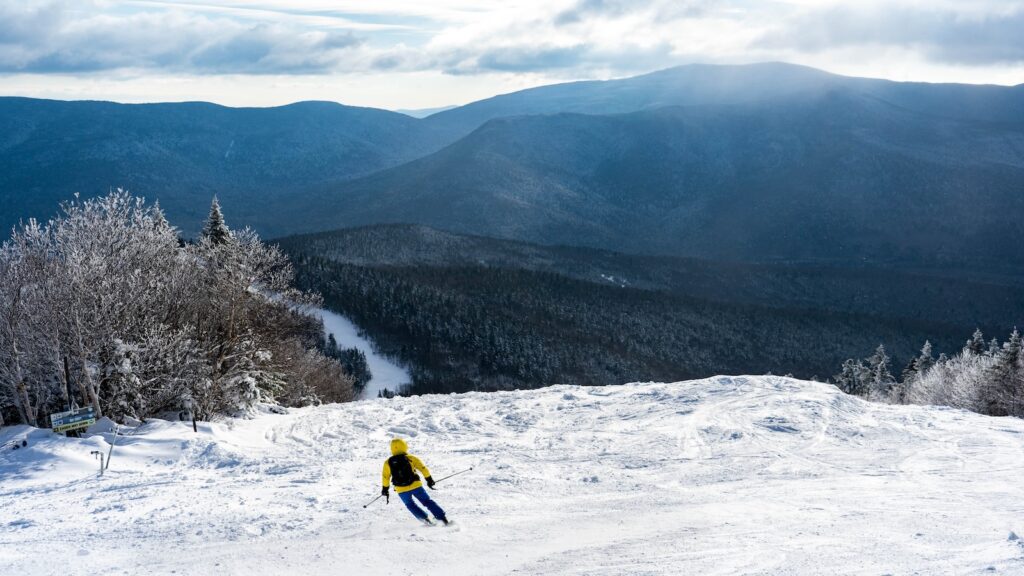 A skier in a yellow jacket going down a ski slope at Waterville Valley.