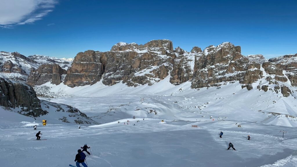 A bunch of skiers going down a slope with jagged mountain views at Cortina d'Ampezzo.