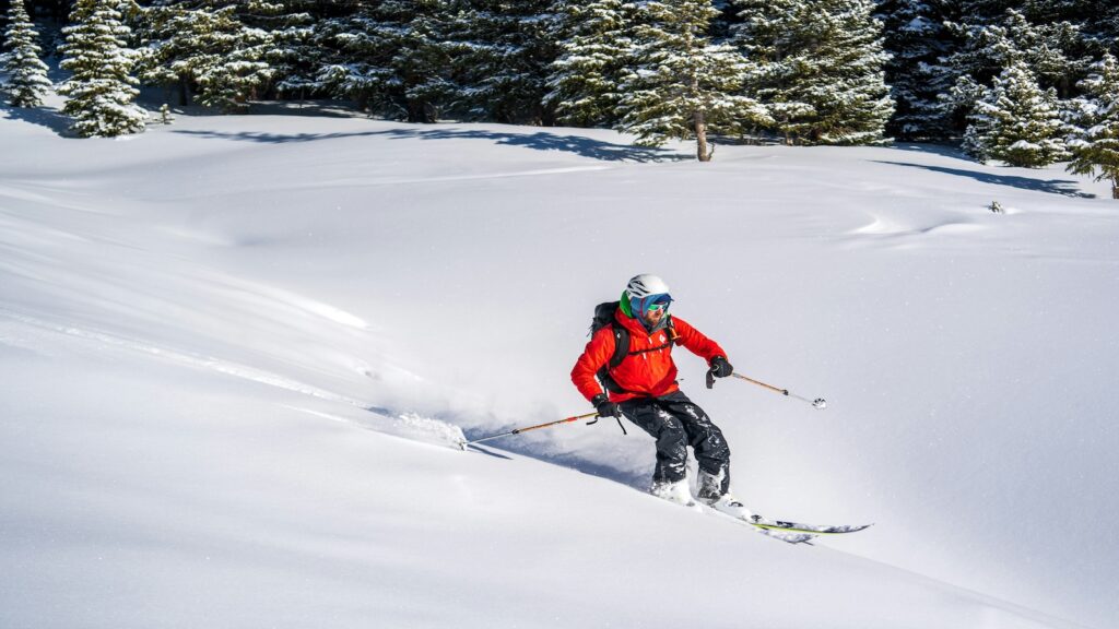 A skier going through fresh powder in a red jacket.