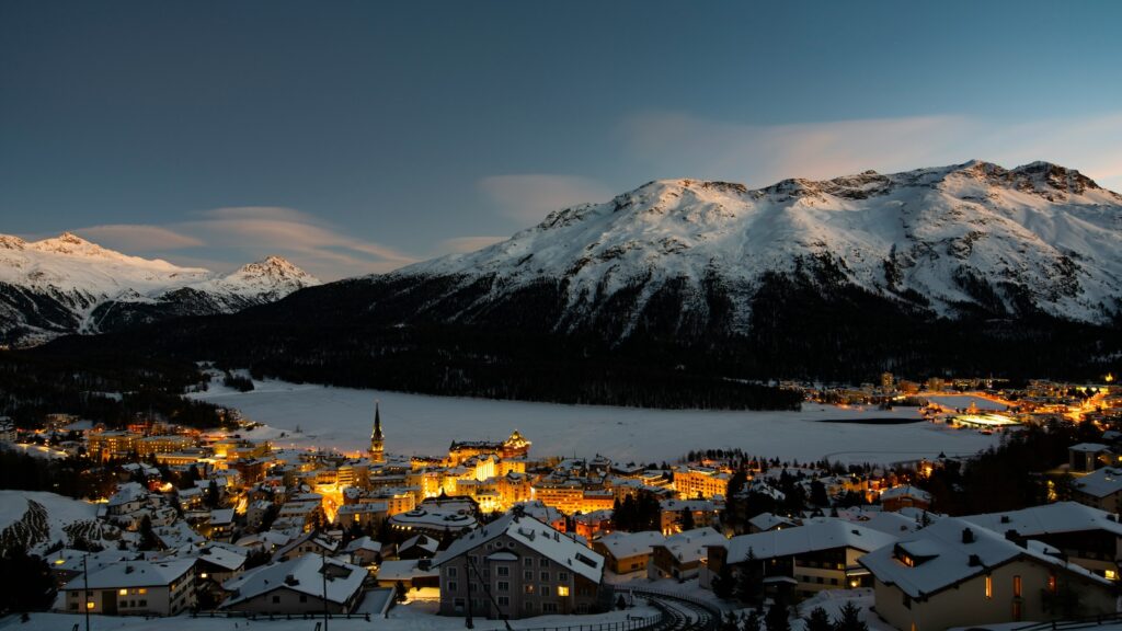 St. Moritz glowing at night surrounded by snowy mountains.